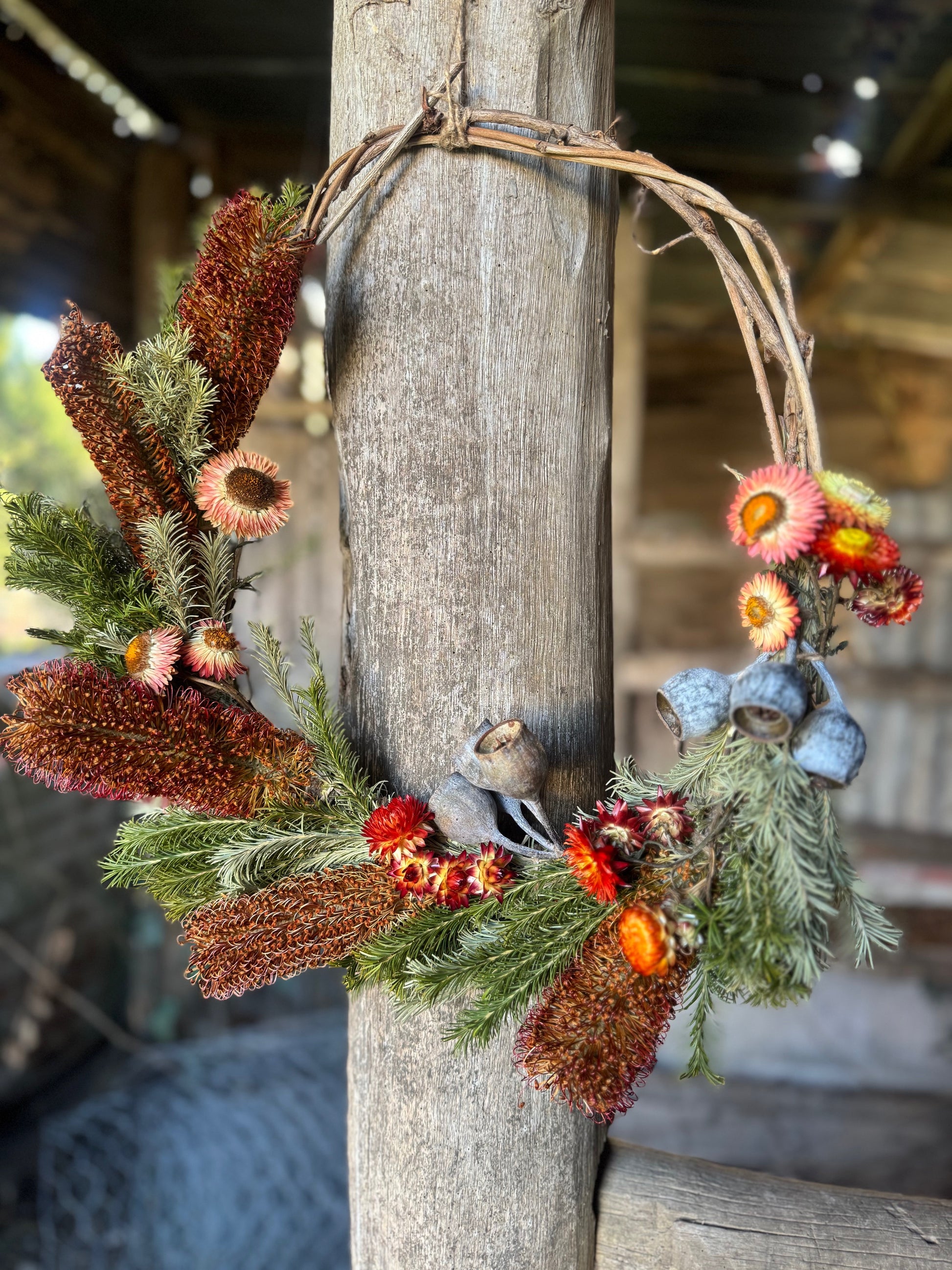 Decorative banksia wreath with flowers and cones hanging on a wooden post.